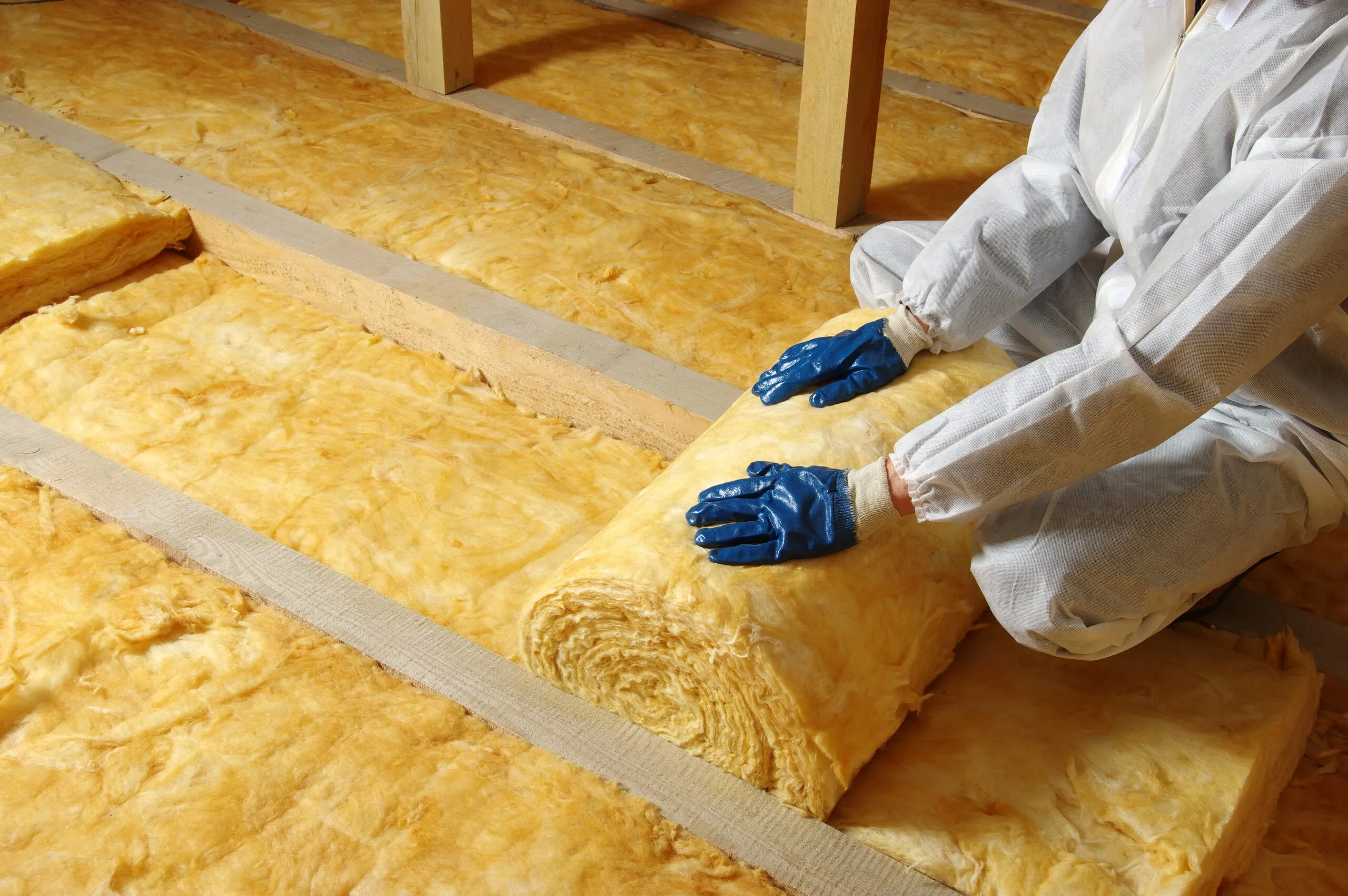 Installer rolling out a batt of fibreglass insulation between attic ceiling joists
