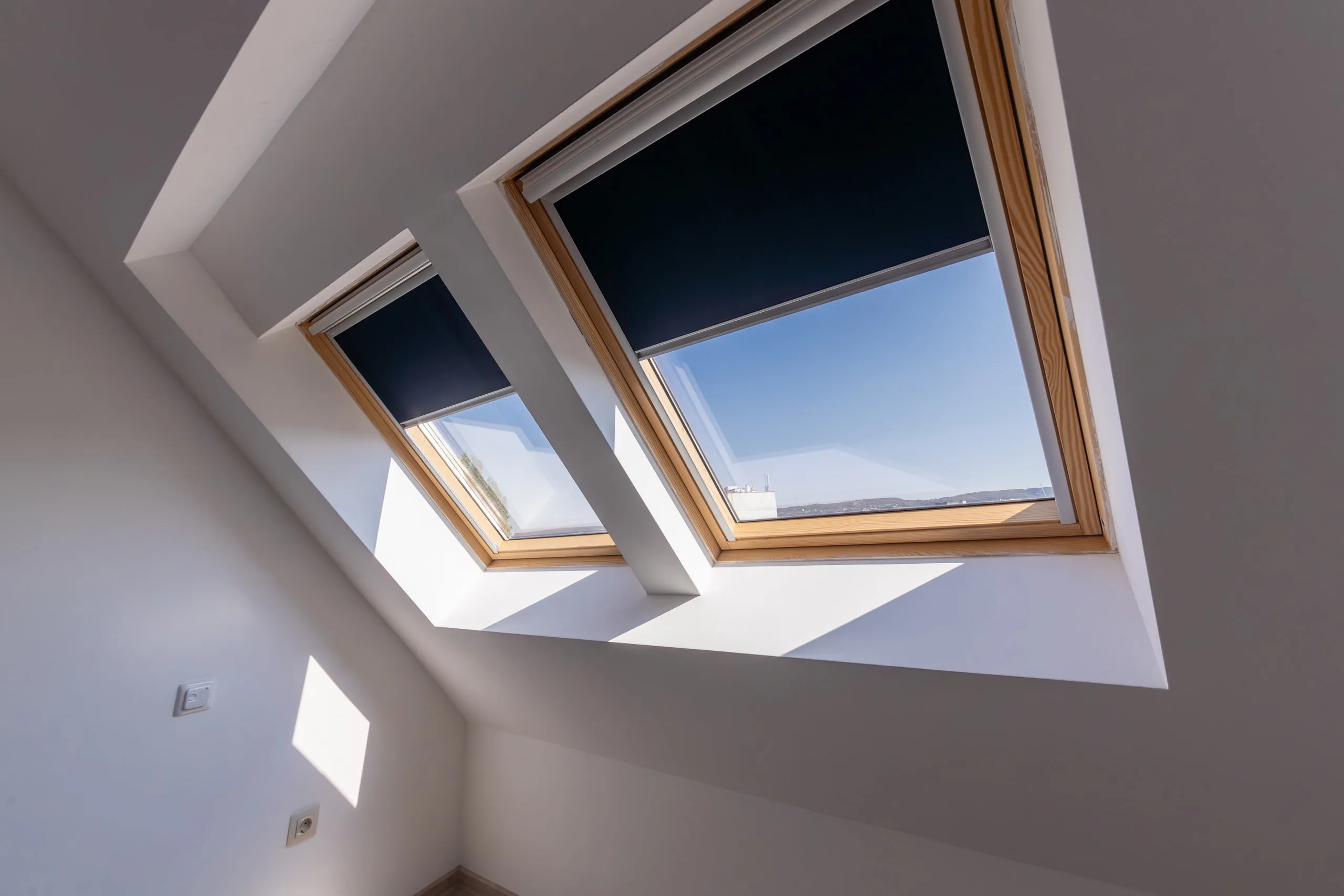 Two skylights set into the sloped ceiling of a finished attic room, blinds half drawn